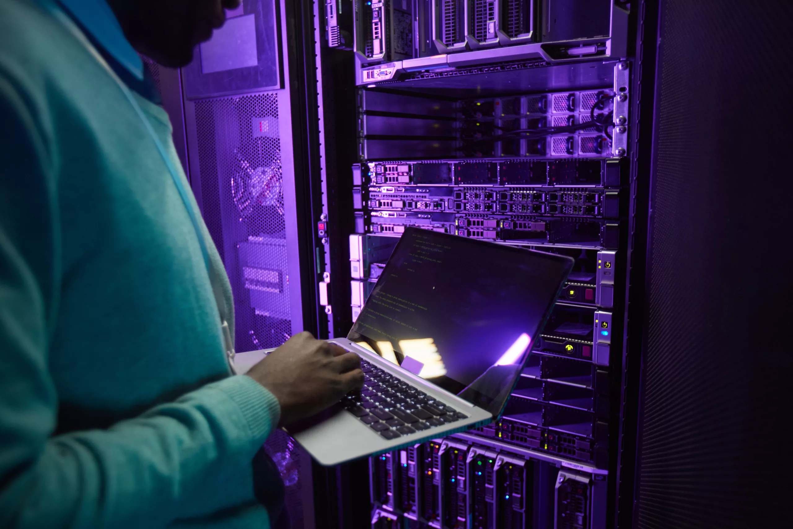 Data engineer holding laptop in front of server