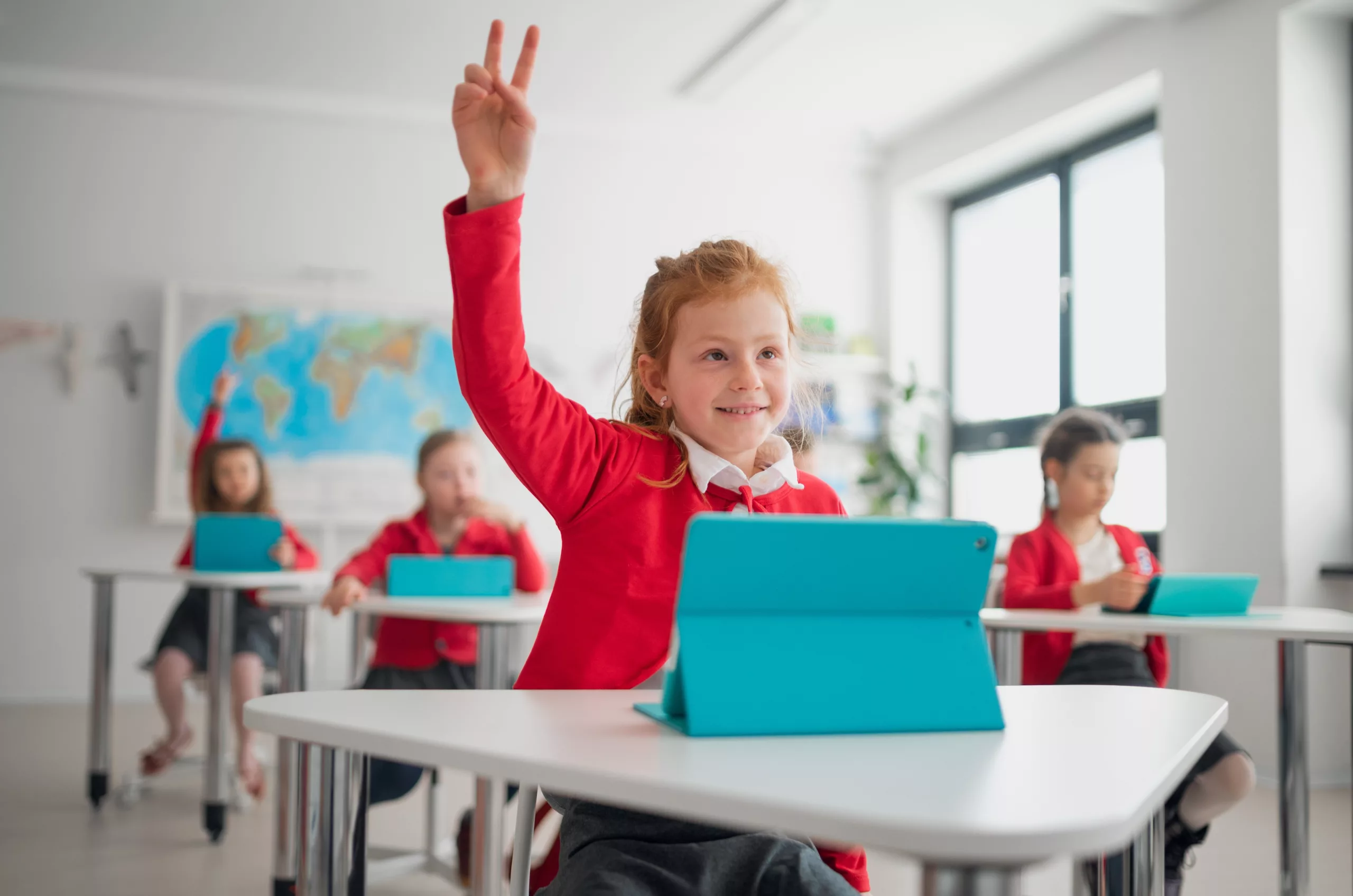 Girl in red jumper holding her hand up in school education classroom